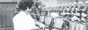 Schwarzweiß-Bild einer Fabrikarbeiterin an einer modernen Maschine.